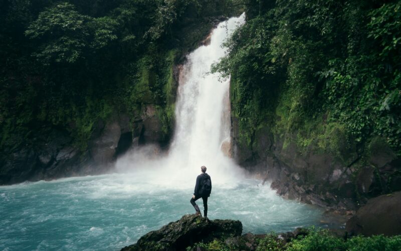 man standing on cliff near falls